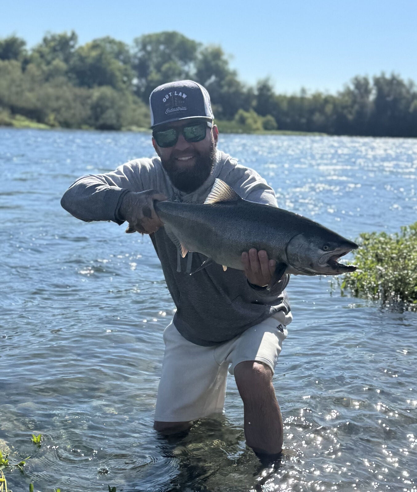 Tournament director Derik Julian kneeling in the Feather River holding a chrome-bright king salmon